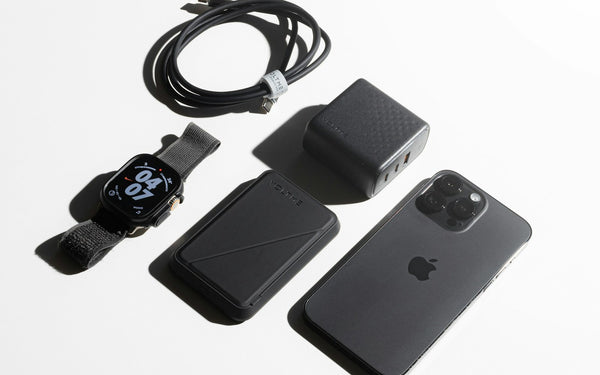 Acessórios de iPhone sobre fundo claro: cabo, carregador, carteira e pulseira